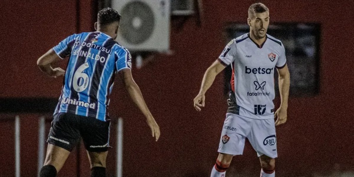 A imagem mostra jogadores dos times de futebol Vitória e Grêmio disputando em campo