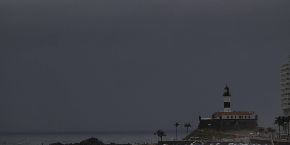 A imagem mostra o Farol da Barra ao fundo com o tempo fechado