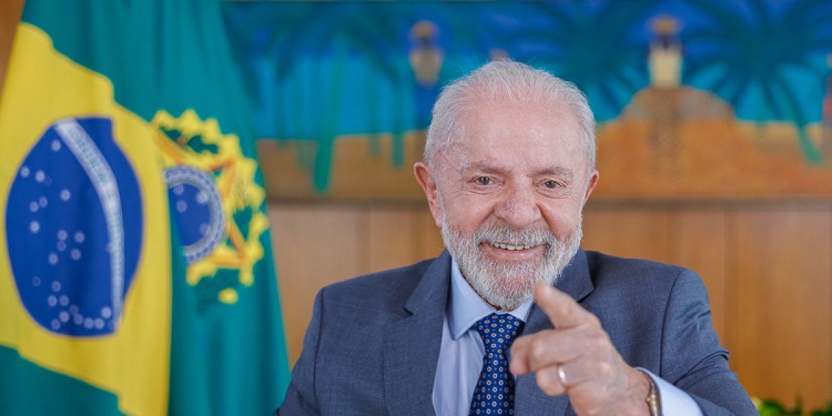 Lula sorrindo em frente a bandeira do Brasil
